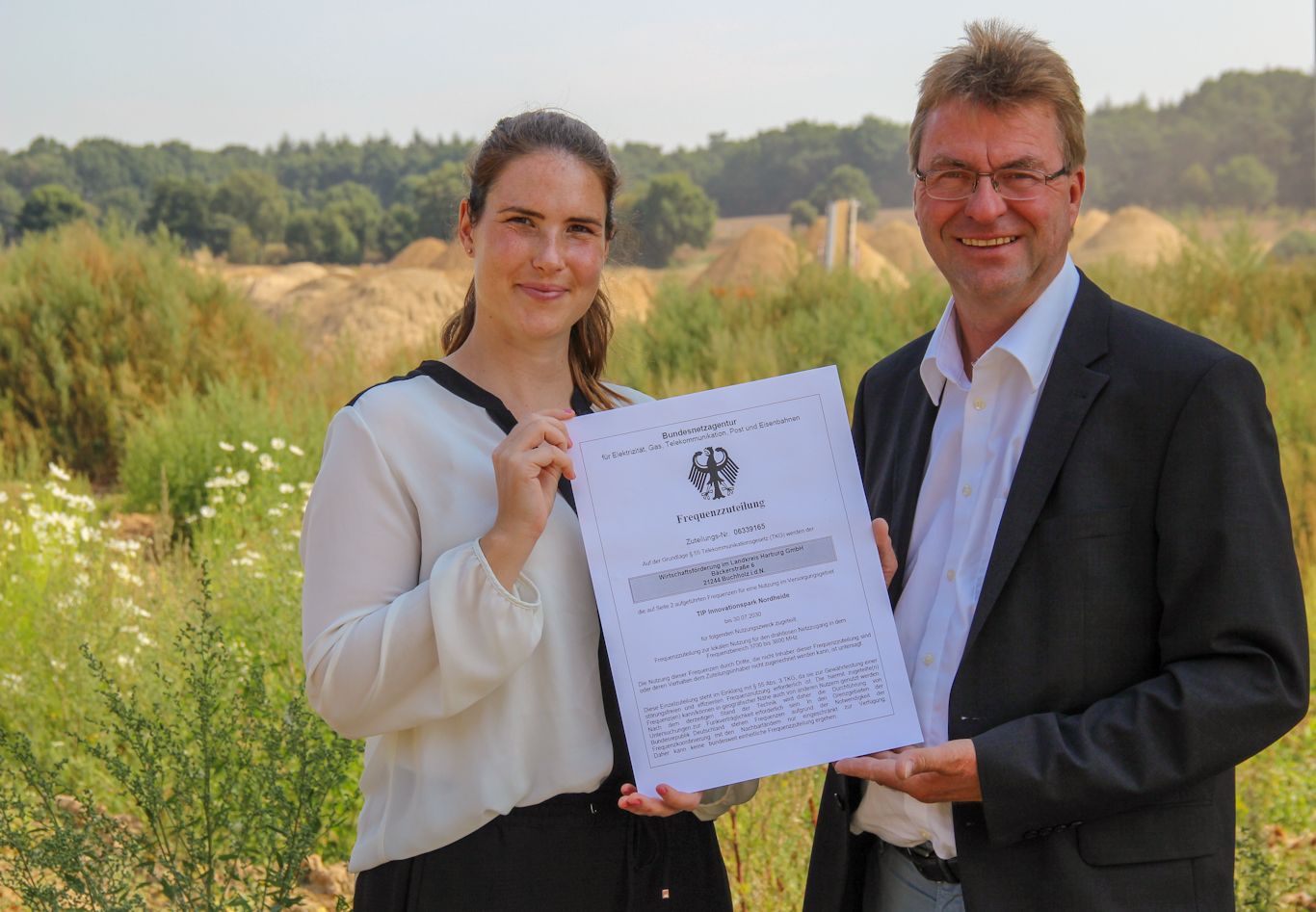 Halten die Urkunde der Bundesnetzagentur für die 5G-Campuslizenz in Händen: WLH-Projektmanagerin Jennifer Coordes und WLH-Geschäftsführer Jens Wrede auf der Baustelle des TIP Innovationspark Nordheide in Buchholz i.d.N.